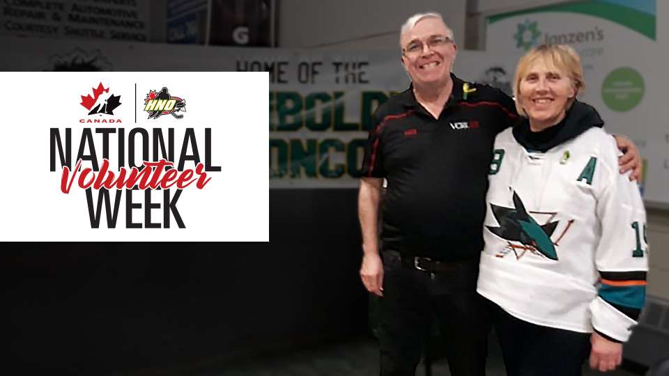 A man and woman standing in front of a hockey jersey during National Volunteer Week.